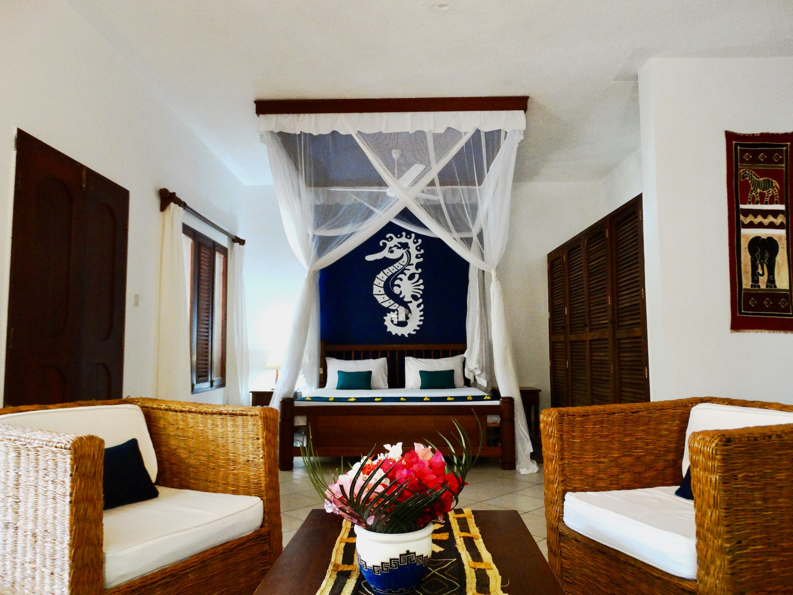 African-decor cottage bedroom with four-poster mosquito net and seahorse mural at Diani Cottages