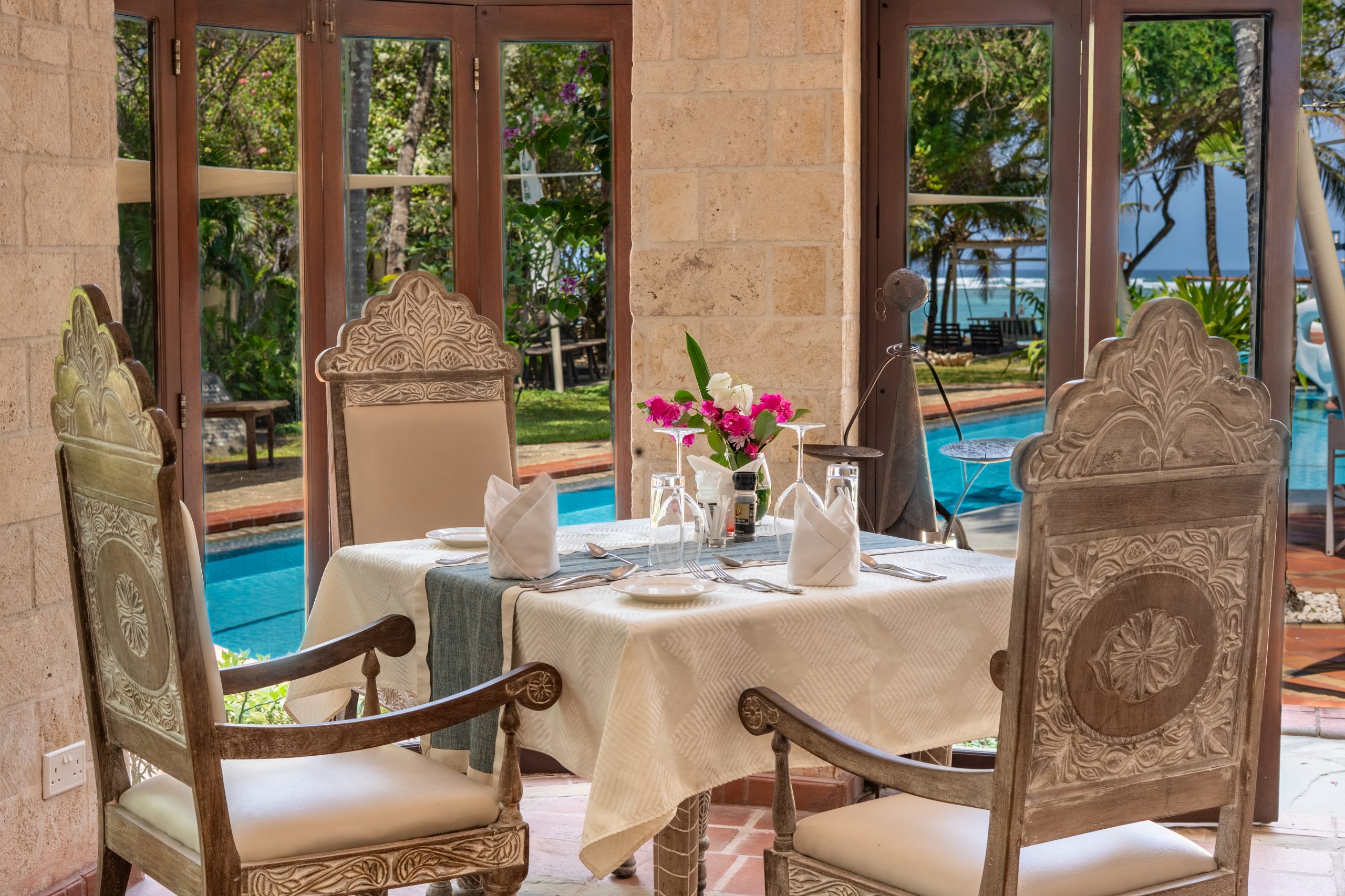 Poolside dining table set for two with ocean and garden views at The Maji Beach